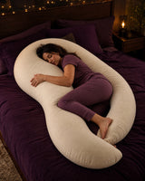 Woman sleeping while hugging an oversized cream crescent body pillow